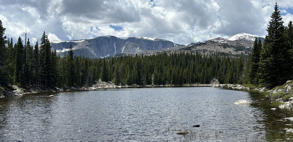 A tranquil alpine lake at Circle Park in the Bighorn Mountains, surrounded by evergreen trees and rugged peaks, perfect for fly fishing the Bighorn Mountains.