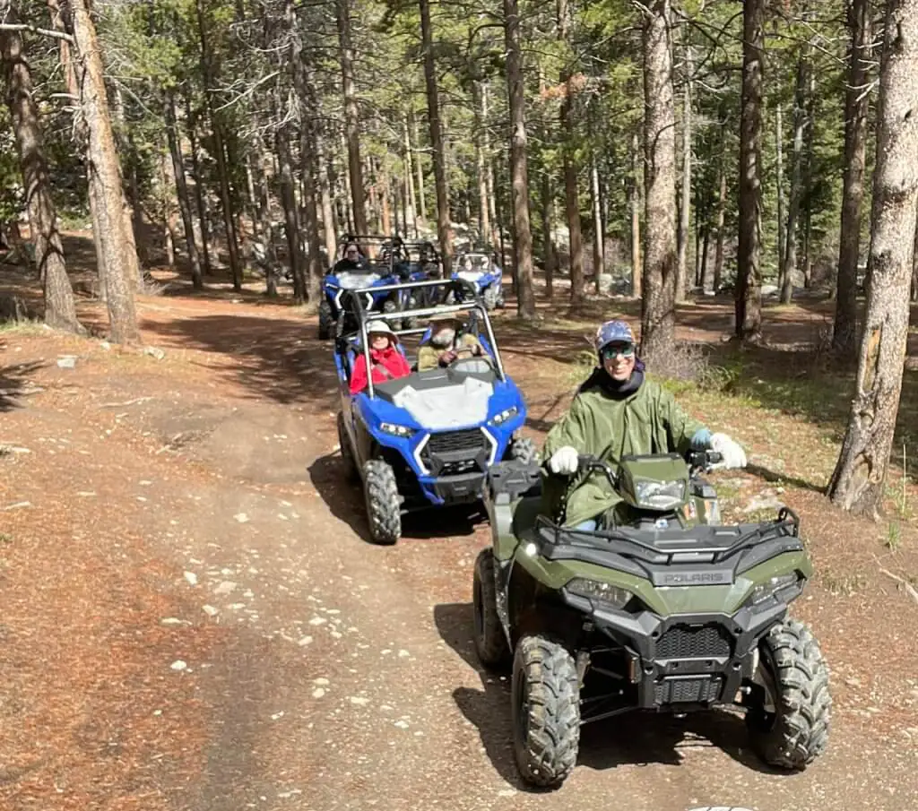 People enjoying one of the best things to do in Buffalo, WY. Taking a ATV guided tour in a forest, riding along a dirt path surrounded by tall pine trees.