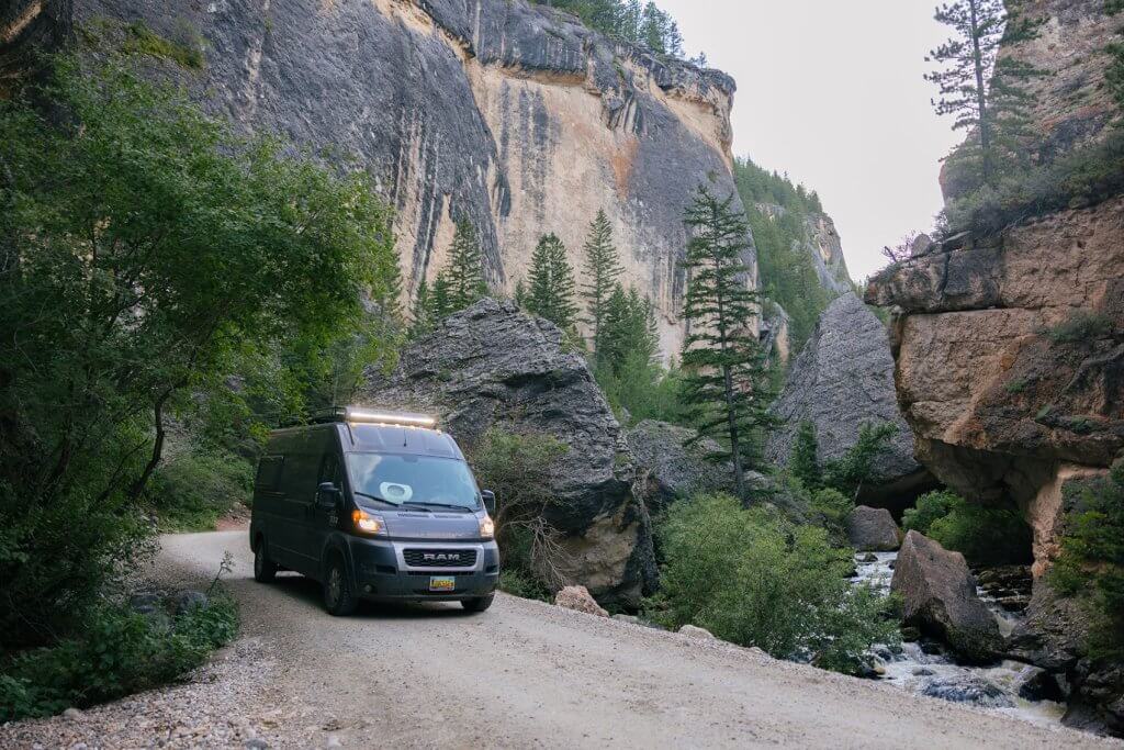 A van driving through Crazy Woman Canyon, surrounded by towering cliffs and lush greenery, a unique thing to for families in Buffalo.