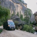 A van driving through Crazy Woman Canyon, surrounded by towering cliffs and lush greenery, a unique thing to for families in Buffalo.