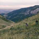 Mountain biking in Buffalo, WY, a top thing to do nearby. Bikers enjoying a scenic trail surrounded by lush landscapes and rugged terrain at sunset.