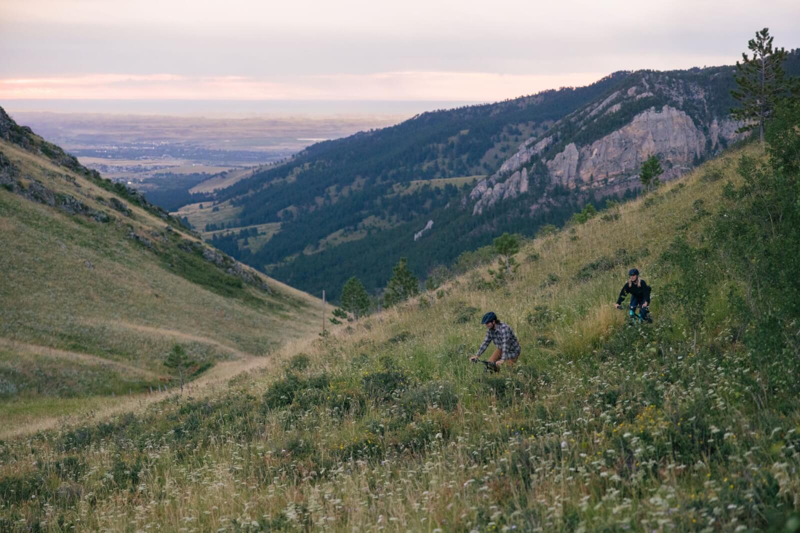 Mountain biking in Buffalo, WY, a top thing to do nearby. Bikers enjoying a scenic trail surrounded by lush landscapes and rugged terrain at sunset.