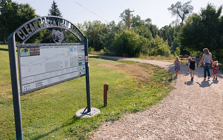 Entrance to the Clear Creek Trail System, one of the best hikes in Buffalo, Wyoming! With a family walking along the scenic path.