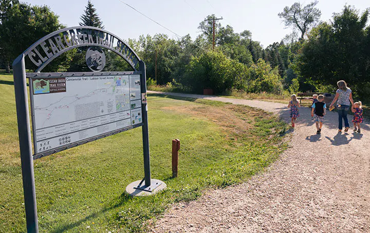 Entrance to the Clear Creek Trail System, one of the best hikes in Buffalo, Wyoming! With a family walking along the scenic path.