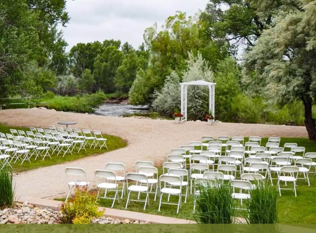 Outdoor event space at Hampton Inn & Suites in Buffalo, Wyoming, featuring a serene riverside setting with chairs arranged for a wedding or special gathering.