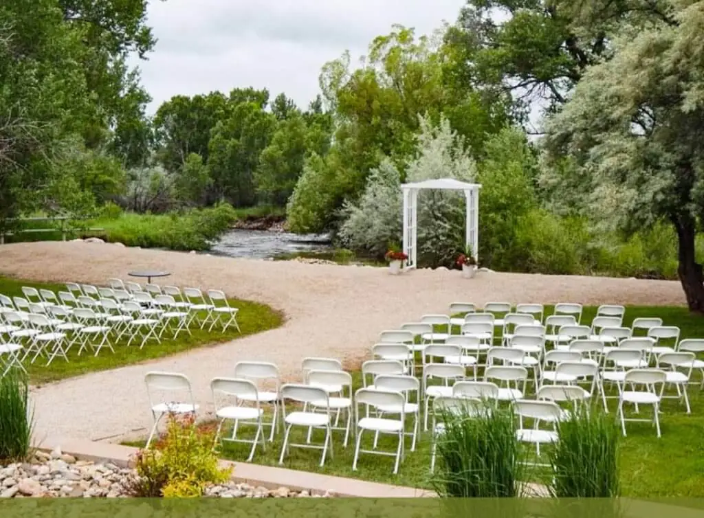 Outdoor event space at Hampton Inn & Suites in Buffalo, Wyoming, featuring a serene riverside setting with chairs arranged for a wedding or special gathering.