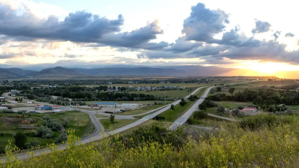 Panoramic view of Johnson County in Buffalo, Wyoming, showcasing rolling hills, highways, and distant mountains under a dramatic sky.