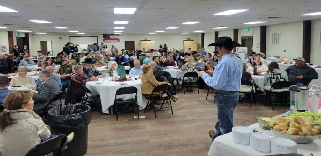 Large gathering at Johnson County Fairgrounds in Buffalo, Wyoming, showcasing a spacious event space with attendees seated at round tables and a presentation in progress.