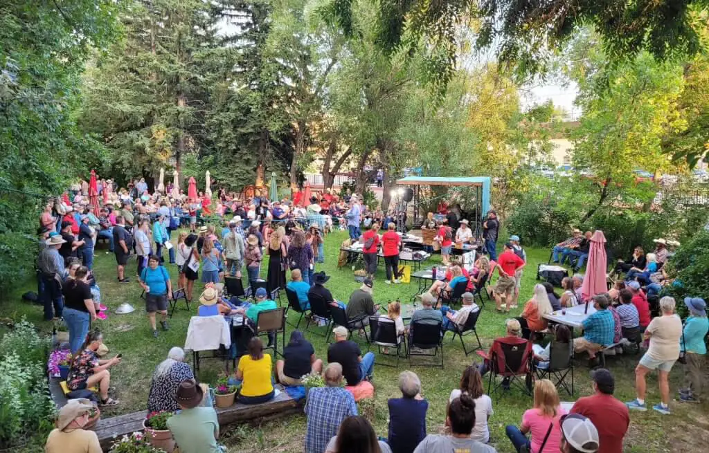 Outdoor event at the Occidental Hotel backyard in Buffalo, Wyoming, with a vibrant crowd gathered in a lush garden setting for a community event.