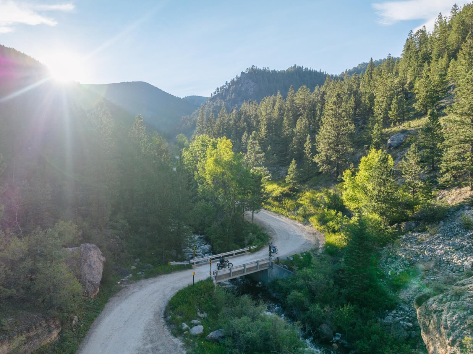 Origins of Crazy Woman Canyon Aerial view of motorcyclists riding through Crazy Woman Canyon alongside a rushing creek and forested mountain slopes in Wyoming.