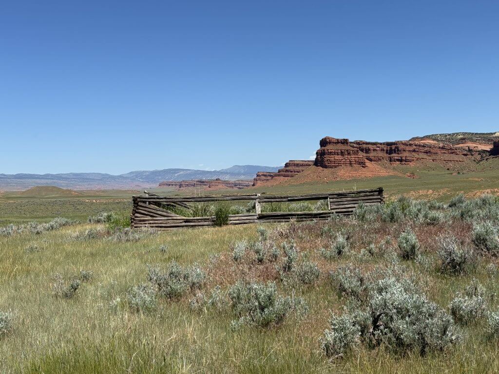 Hole in the Wall Hole in the Wall Wyoming landscape showing weathered wooden fence in sagebrush prairie with red rock formations and distant mountains under clear blue sky