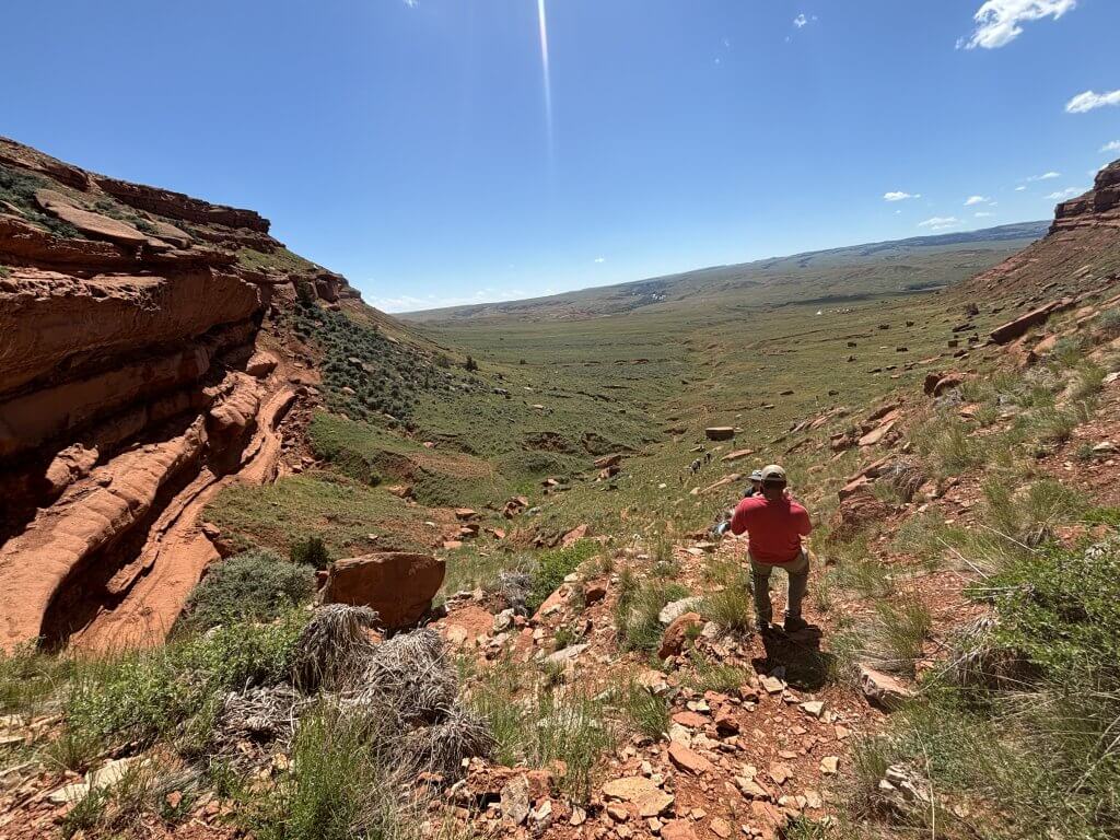 Hole in the Wall Hole-in-the-Wall Trailhead & Viewpoint featuring visitor enjoying panoramic desert landscape view with layered sandstone cliffs and grassland valley
