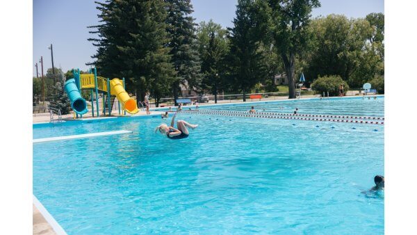 20 Free and Budget-Friendly Things to Do in Buffalo, Wyoming Children playing at the Buffalo Municipal Swimming Pool in Wyoming, with a girl mid-air after jumping off the diving board and colorful water slides in the background.