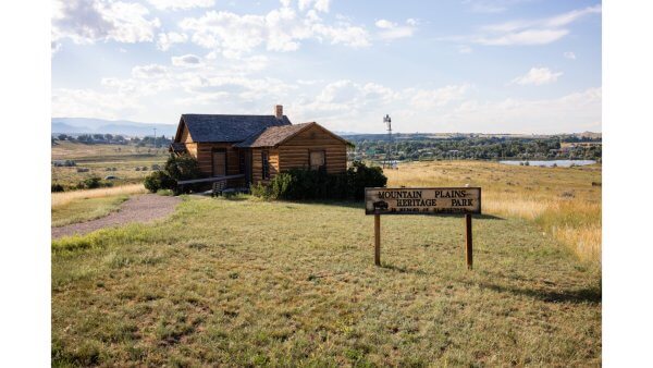 20 Free and Budget-Friendly Things to Do in Buffalo, Wyoming Rustic log cabin at Mountain Plains Heritage Park in Buffalo, Wyoming, with a wooden sign in the foreground and panoramic views of rolling hills.