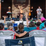 Audience enjoying a live outdoor concert in lawn chairs at Crazy Woman Square in Buffalo, Wyoming, with musicians performing on stage under a summer evening sky.