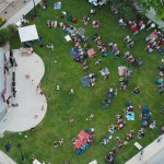 A community crowd enjoying live music and sunshine on the lawn at Crazy Woman Square.