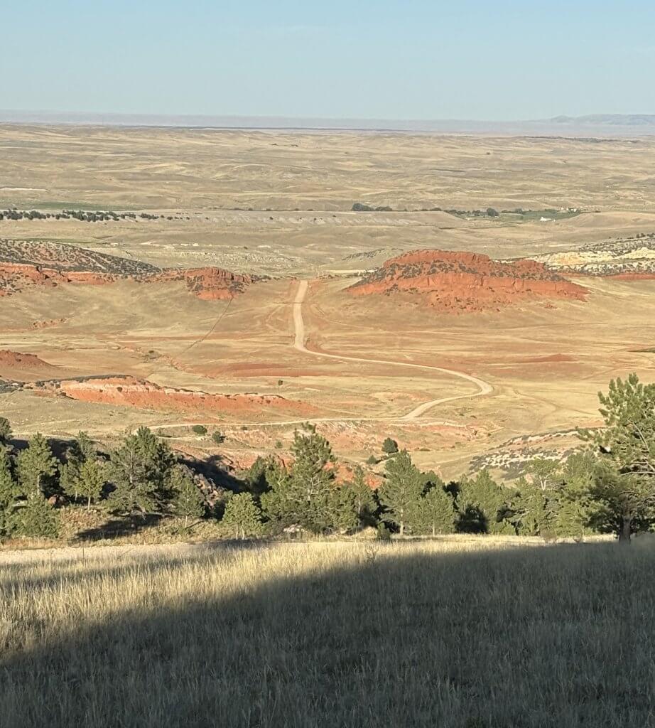 Hole in the Wall Slip Road winding through expansive Wyoming high desert landscape with red rock formations and golden grassland