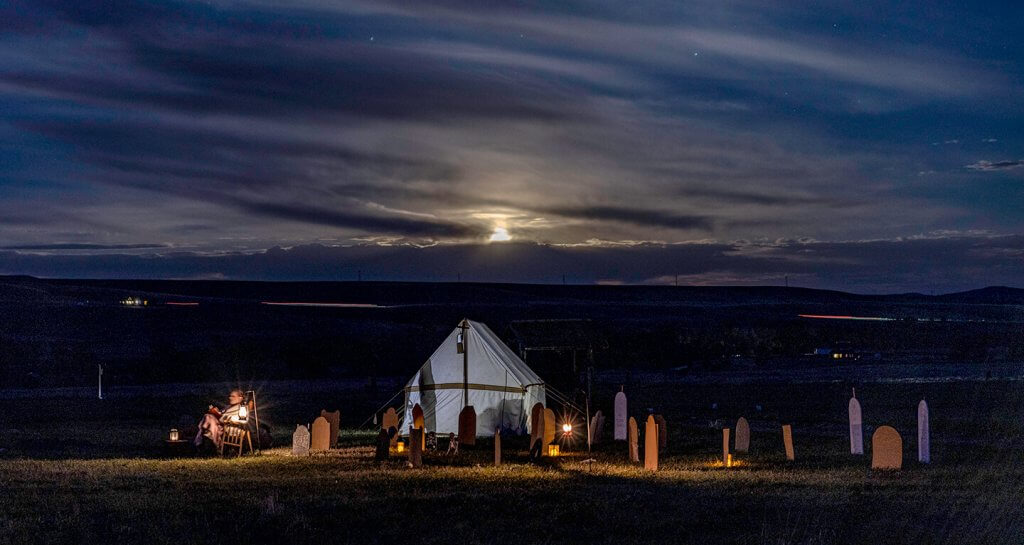 A white tent in a graveyard with a light in the background at Fort Phil Kearny.