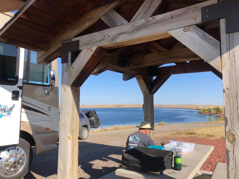 A guest sitting at a picnic table along side their camper and SUV next to the water